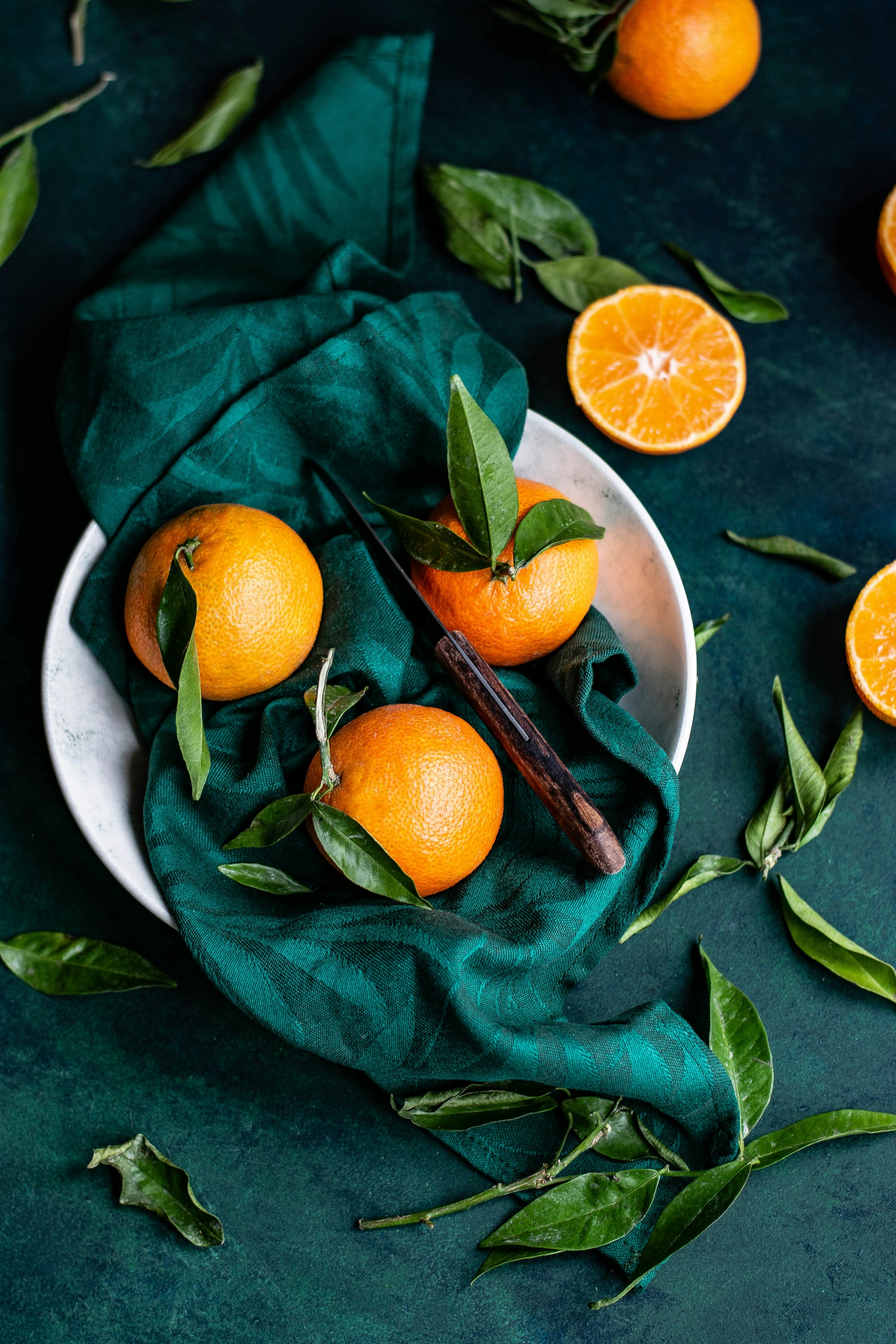 Fresh oranges and green leaves on deep emerald fabric